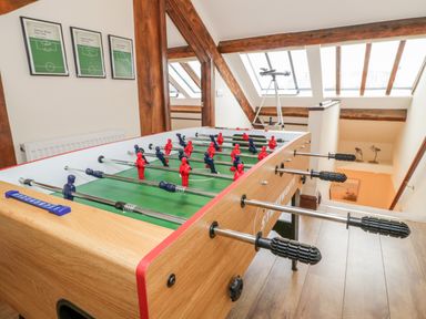 A room with a foosball table under skylight windows and wooden beams with framed pictures on the wall and a telescope near the windows at Seion Chapel in Beaumaris