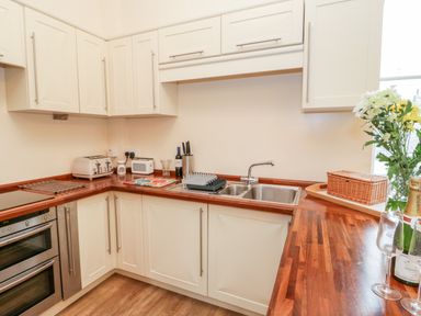 A kitchen with white cabinets wooden countertops a double sink toaster knives and flowers on the counter at Seion Chapel Beaumaris