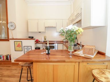 A kitchen with wooden countertops white cabinets two bar stools a vase with flowers and a bottle of champagne with glasses at Seion Chapel in Beaumaris
