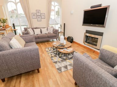A living room with gray sofas a wall mounted TV a geometric patterned rug and round wooden coffee tables at Seion Chapel in Beaumaris