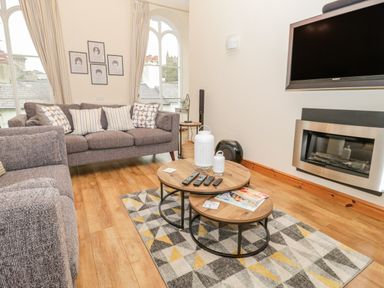 A living room with two grey sofas a wooden coffee table with remotes and magazines a wall-mounted TV and a fireplace at Seion Chapel in Beaumaris