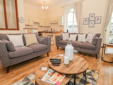 A living room with two gray sofas and a wooden coffee table in front of a kitchen at Seion Chapel in Beaumaris