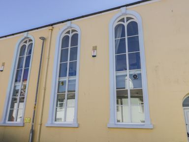 The exterior of a building with three tall arched windows and a pale yellow wall at Seion Chapel in Beaumaris