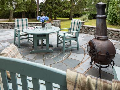 An outdoor patio with a round table and two chairs with cushions a bench and a metal outdoor fireplace at Waterhead Cottage in Ecclerigg near Troutbeck Bridge