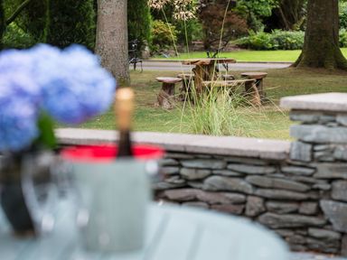 An outdoor garden area with wooden stools and table surrounded by trees and grass at Waterhead Cottage Ecclerigg near Troutbeck Bridge