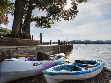 Two kayaks on a shore near a wooden dock with trees and a body of water at Waterhead Cottage Ecclerigg near Troutbeck Bridge