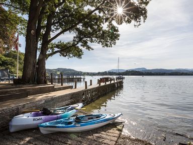 A lakeside view with two kayaks on the shore near a wooden pier and trees at Waterhead Cottage Ecclerigg near Troutbeck Bridge