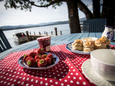 An outdoor table set with strawberries scones jam and a cup near a lake at Waterhead Cottage in Ecclerigg near Troutbeck Bridge