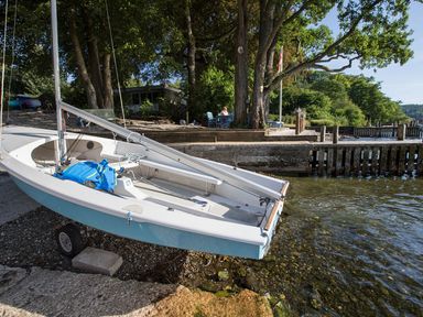 A small sailboat on a shore next to a lake with trees and a dock in the background at Waterhead Cottage Ecclerigg near Troutbeck Bridge