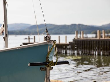 The bow of a blue boat tied with rope near a wooden dock on a lake with hills in the background at Waterhead Cottage in Ecclerigg near Troutbeck Bridge