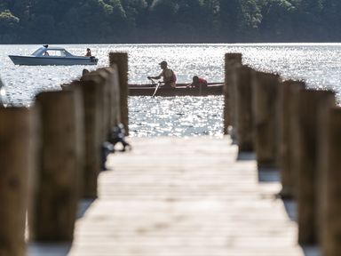 A wooden pier leading to a lake with two boats and people on the water at Waterhead Cottage in Ecclerigg near Troutbeck Bridge