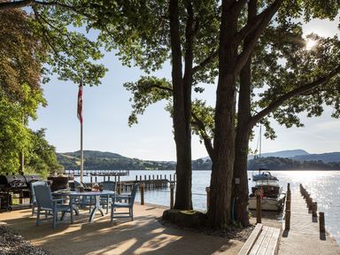 A lakeside outdoor dining area with a table and chairs near boats docked at a wooden pier at Waterhead Cottage in Ecclerigg near Troutbeck Bridge