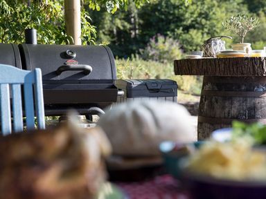 An outdoor barbecue grill near a wooden barrel table with plates and glasses at Waterhead Cottage Ecclerigg near Troutbeck Bridge