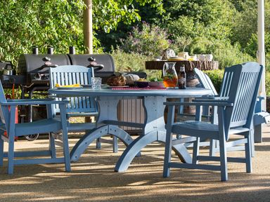 An outdoor dining area with blue wooden chairs and a round table with food and drinks near a barbecue grill at Waterhead Cottage in Ecclerigg near Troutbeck Bridge