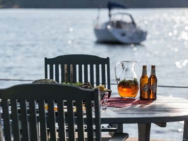 An outdoor dining table with chairs bread a pitcher and two bottles with water and a boat in the background at Waterhead Cottage Ecclerigg near Troutbeck Bridge