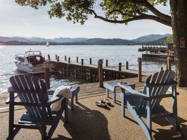 A lakeside seating area with two wooden chairs and a dock with boats at Waterhead Cottage in Ecclerigg near Troutbeck Bridge