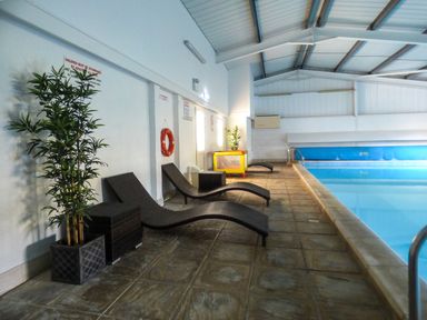 An indoor swimming pool area with lounge chairs plants and safety equipment at Hazel Cottage in Poughill near Bude