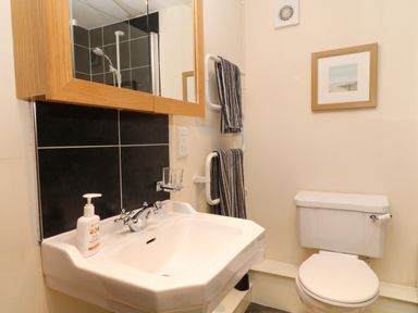 A bathroom with a white sink a toilet two striped towels on a rail a mirror above the sink and a framed picture on the wall at Hazel Cottage in Poughill near Bude