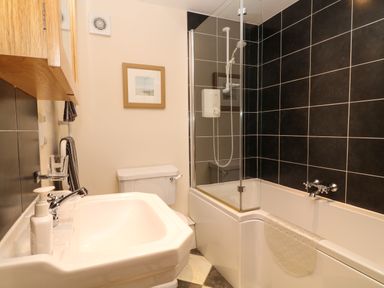 A bathroom with a sink a toilet a bathtub with a shower and black tiled walls at Hazel Cottage in Poughill near Bude
