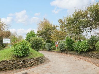 A driveway flanked by stone walls and bushes with signs for Trevalgas Cottages and a speed limit at Hazel Cottage in Poughill near Bude