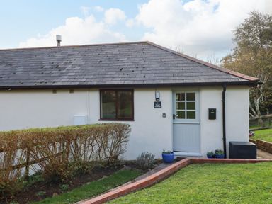 Exterior view of a single-story building with a white door window and hedges in front at Hazel Cottage in Poughill near Bude