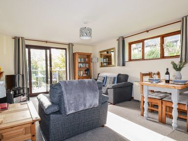 A living room with sofas a wooden dining table bookshelf and sliding glass doors at Hazel Cottage in Poughill near Bude