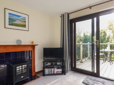 A living room corner with a black TV on a stand and a fireplace next to a sliding glass door opening to a balcony at Hazel Cottage in Poughill near Bude