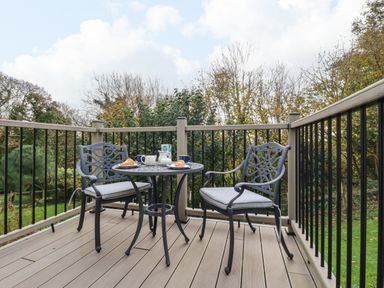 A balcony with two metal chairs and a round table with breakfast items surrounded by trees at Hazel Cottage in Poughill near Bude