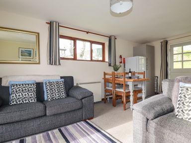 A living room with two gray sofas a dining table with four chairs a refrigerator and a window at Hazel Cottage in Poughill near Bude