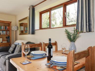 A dining table set with plates glasses and a bottle of wine next to a sofa and bookshelf at Hazel Cottage in Poughill near Bude