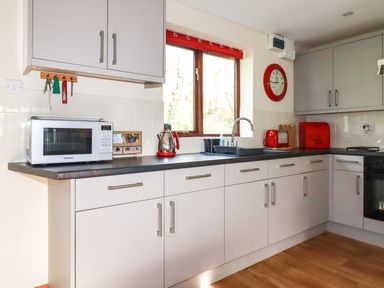 A kitchen with white cabinets red appliances a microwave and a window at Hazel Cottage in Poughill near Bude