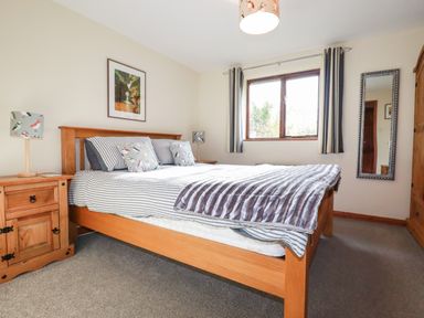 A bedroom with a wooden bed, bedside tables, a window with curtains, and a wall mirror at Hazel Cottage in Poughill near Bude