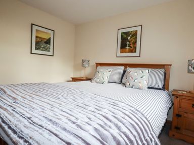 A bedroom with a double bed striped bedding and bird patterned pillows two bedside tables with lamps and framed pictures on the wall at Hazel Cottage in Poughill near Bude