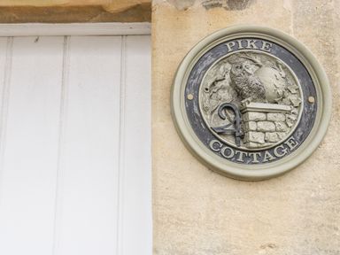 A circular plaque with an owl sculpture and the words Pike Cottage on a stone wall at Pike Cottage in Acton Turville near Chipping Sodbury