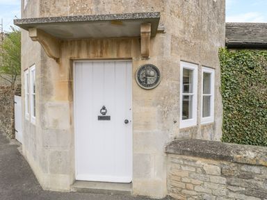 The exterior entrance door of a stone cottage with a white wooden door and two white-framed windows at Pike Cottage in Acton Turville near Chipping Sodbury