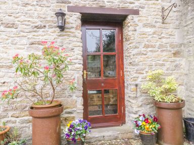 A wooden door on a stone wall with potted plants on either side at Pike Cottage in Acton Turville near Chipping Sodbury