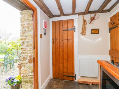 Entryway with wooden door and stone wall opening to garden with green metal chairs at Pike Cottage in Acton Turville near Chipping Sodbury