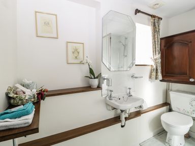 A bathroom with a sink mirror toilet wooden shelves and framed pictures at Pike Cottage in Acton Turville near Chipping Sodbury