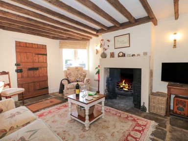A living room with a fireplace television wooden door and floral furniture at Pike Cottage in Acton Turville near Chipping Sodbury
