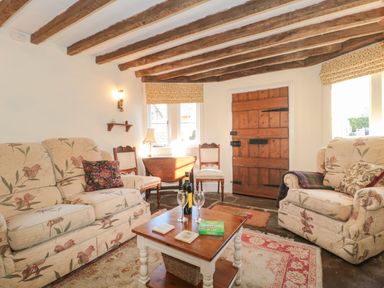 A sitting room with floral sofas a wooden table and wooden door at Pike Cottage in Acton Turville near Chipping Sodbury
