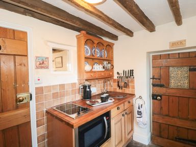 A kitchen with wooden cabinets and beams a microwave and tea on the counter at Pike Cottage in Acton Turville near Chipping Sodbury