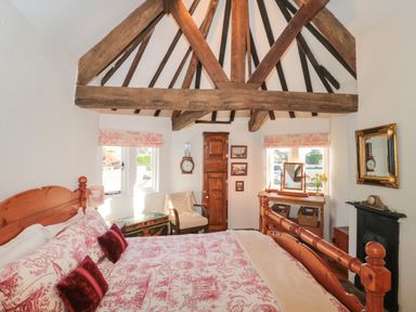 A bedroom with wooden bed frame and exposed ceiling beams at Pike Cottage in Acton Turville near Chipping Sodbury