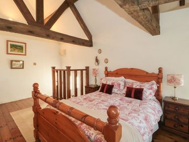 A bedroom with a wooden bed and bedside tables under exposed ceiling beams at Pike Cottage in Acton Turville near Chipping Sodbury