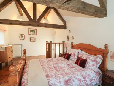 A bedroom with wooden bed frame and floral bedding under exposed wooden beams at Pike Cottage in Acton Turville near Chipping Sodbury