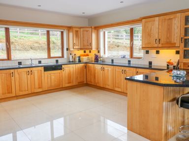 A kitchen with wooden cabinets black countertops and large windows at Rossanean in Farranfore near Killarney County Kerry