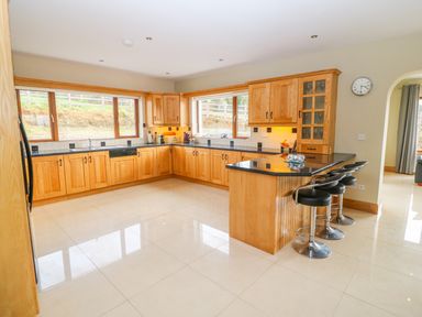 A kitchen with wooden cabinets black countertops three black bar stools and large windows at Rossanean in Farranfore near Killarney County Kerry
