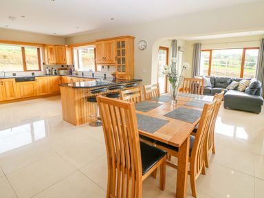 An open kitchen and dining area with wooden cabinets a dining table with chairs and a black leather sofa at Rossanean Farranfore near Killarney County Kerry