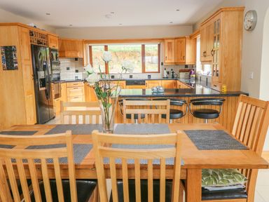 A kitchen with a wooden dining table and chairs a vase with white flowers on the table and wooden cabinets and black countertops at Rossanean in Farranfore near Killarney County Kerry
