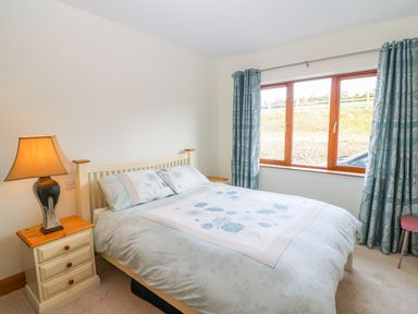 A bedroom with a bed a bedside table with a lamp and a window with curtains at Rossanean in Farranfore near Killarney County Kerry