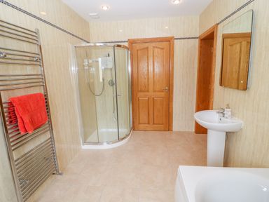 A bathroom with a curved glass shower enclosure a pedestal sink a wall mirror wooden doors and a heated towel rail with a red towel at Rossanean in Farranfore near Killarney County Kerry